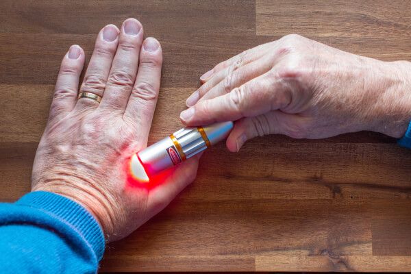 Elder using red light therapy to treat hand arthritis