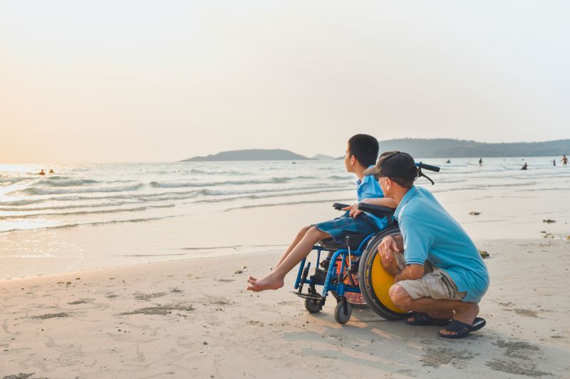 man-with-child-in-wheelchair-on-beach