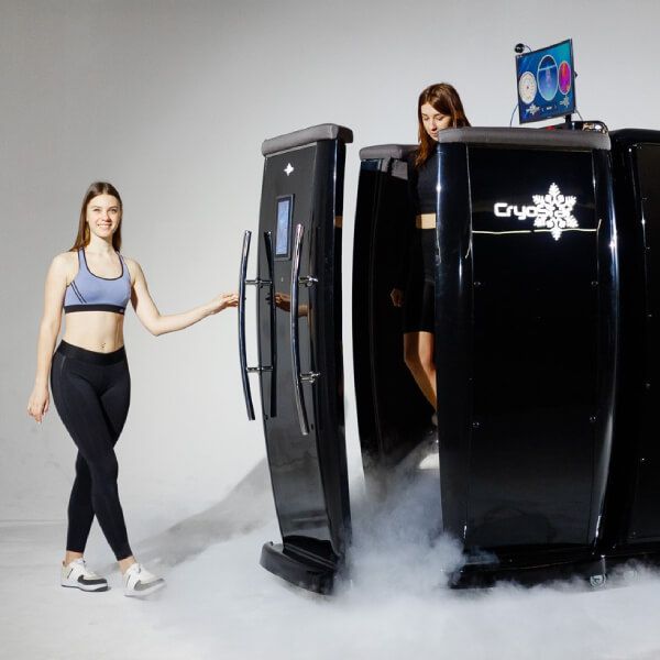 Woman helping another woman get outside of a cryotherapy chamber at a medical facility